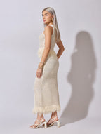 Woman wearing a white crochet dress with fringe details on a plain background