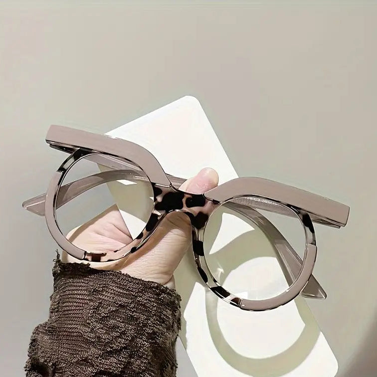 Metallic cat-eye glasses held by a hand against a neutral background