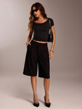 Woman wearing a black outfit with a cropped top and wide-leg pants against a neutral background