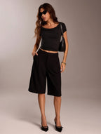 Woman wearing a black outfit with a cropped top and wide-leg pants against a neutral background