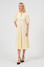 Woman wearing a light yellow dress with puff sleeves on a white background