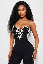 Woman wearing a black strapless jumpsuit with white embroidery on a white background
