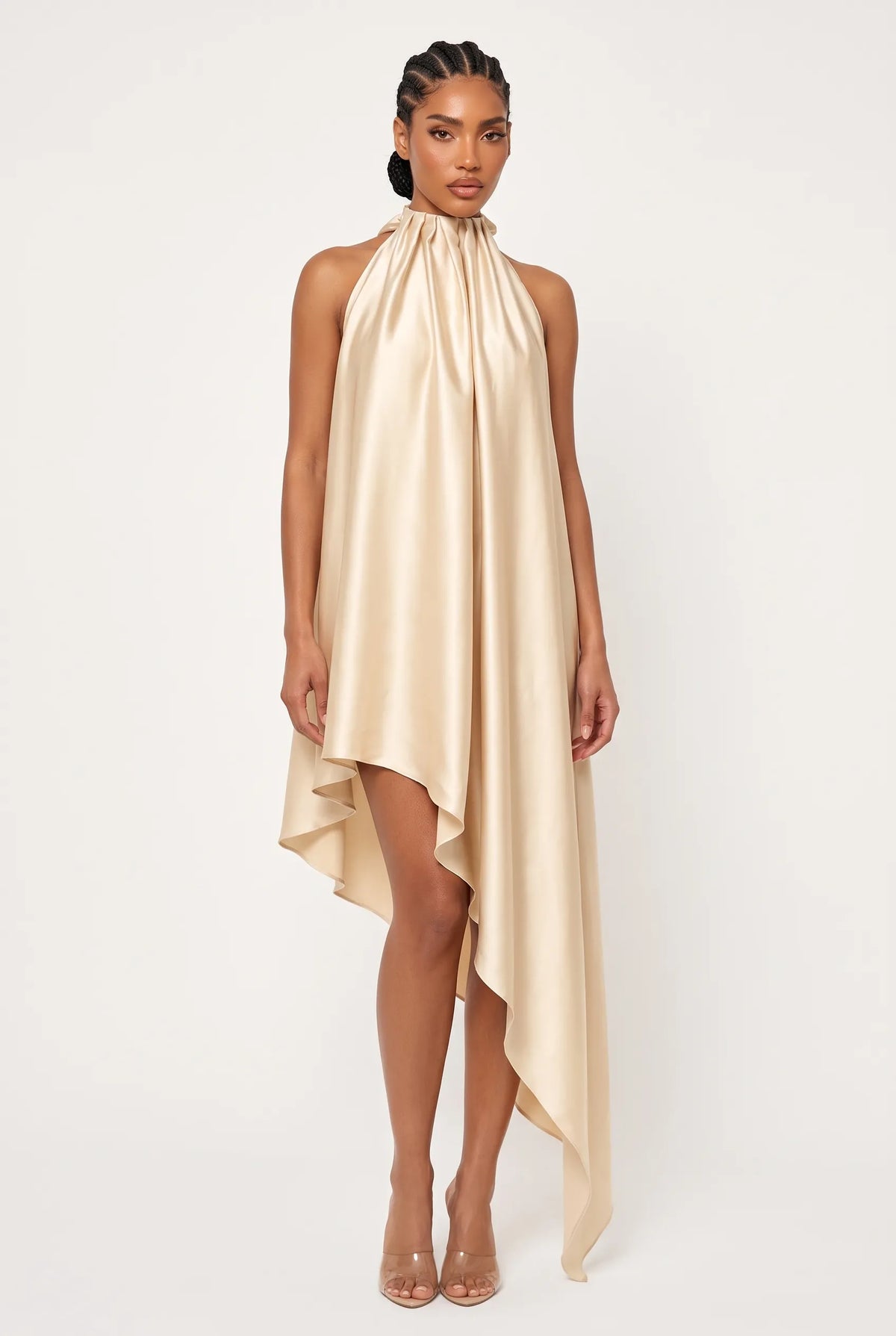 A model wearing a champagne-colored high-neck halter dress with an asymmetrical draped hem, photographed against a plain white studio background.