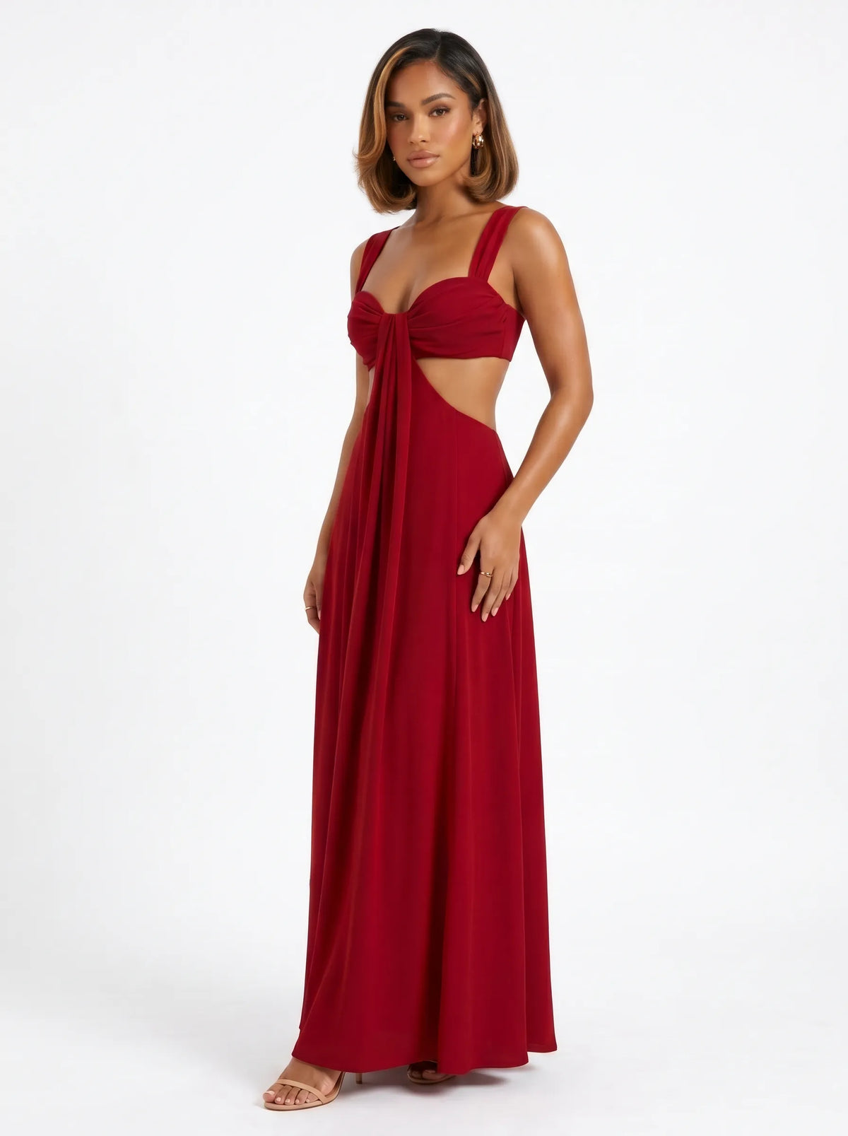 The dress shown is a crimson red maxi dress featuring side cutouts at the waist, a structured sweetheart bustier top with gathered drape detail, wide shoulder straps, and a bow tie backclosure.