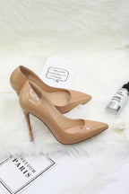 Beige high-heeled shoes on a white fur surface with a small bottle and text card.