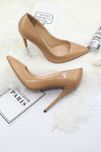 Beige high-heeled shoes on a white surface with a small bottle and text in the background.