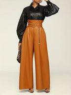 Person wearing a black shirt and brown leather pants on a plain background