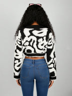Person wearing a black and white patterned sweater and blue jeans on a gray background