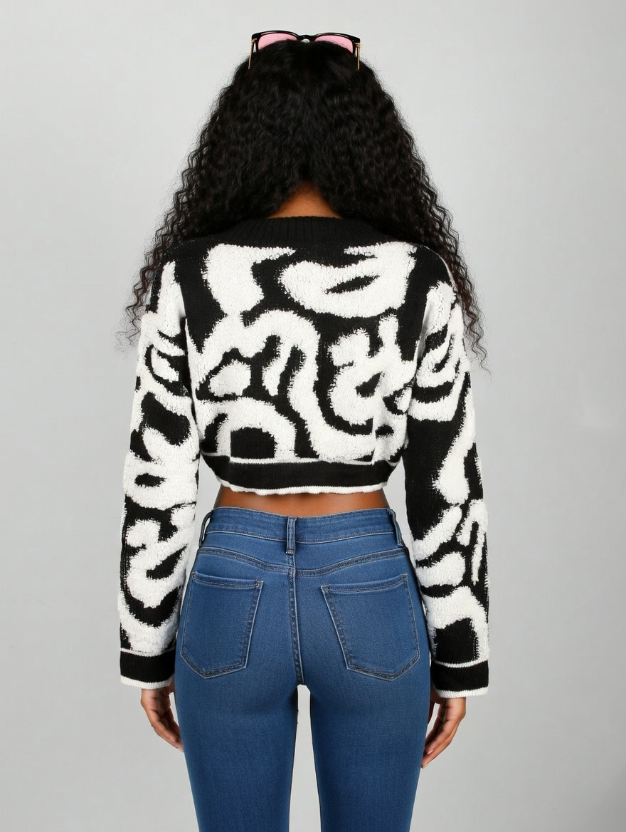 Person wearing a black and white patterned sweater and blue jeans on a gray background