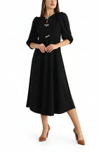Woman wearing a black dress with white buttons on a light background