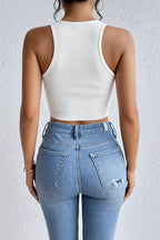 a woman wearing a white, sleeveless, crop top paired with washed jeans on a natural background