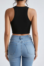 a woman wearing a black, sleeveless, crop top paired with washed jeans on a natural background