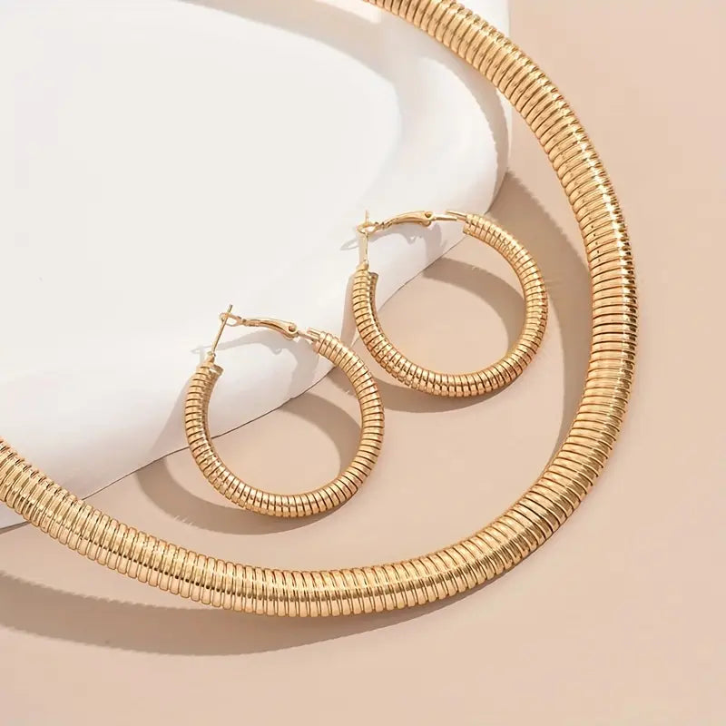 Gold necklace and hoop earrings on a beige surface