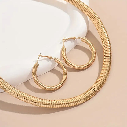 Gold necklace and hoop earrings on a beige surface