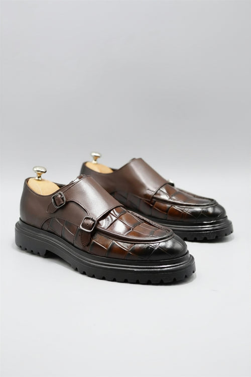 Pair of brown leather shoes with a buckle on a light gray background