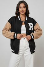 Woman wearing a black and beige varsity jacket with 'R' on a plain background