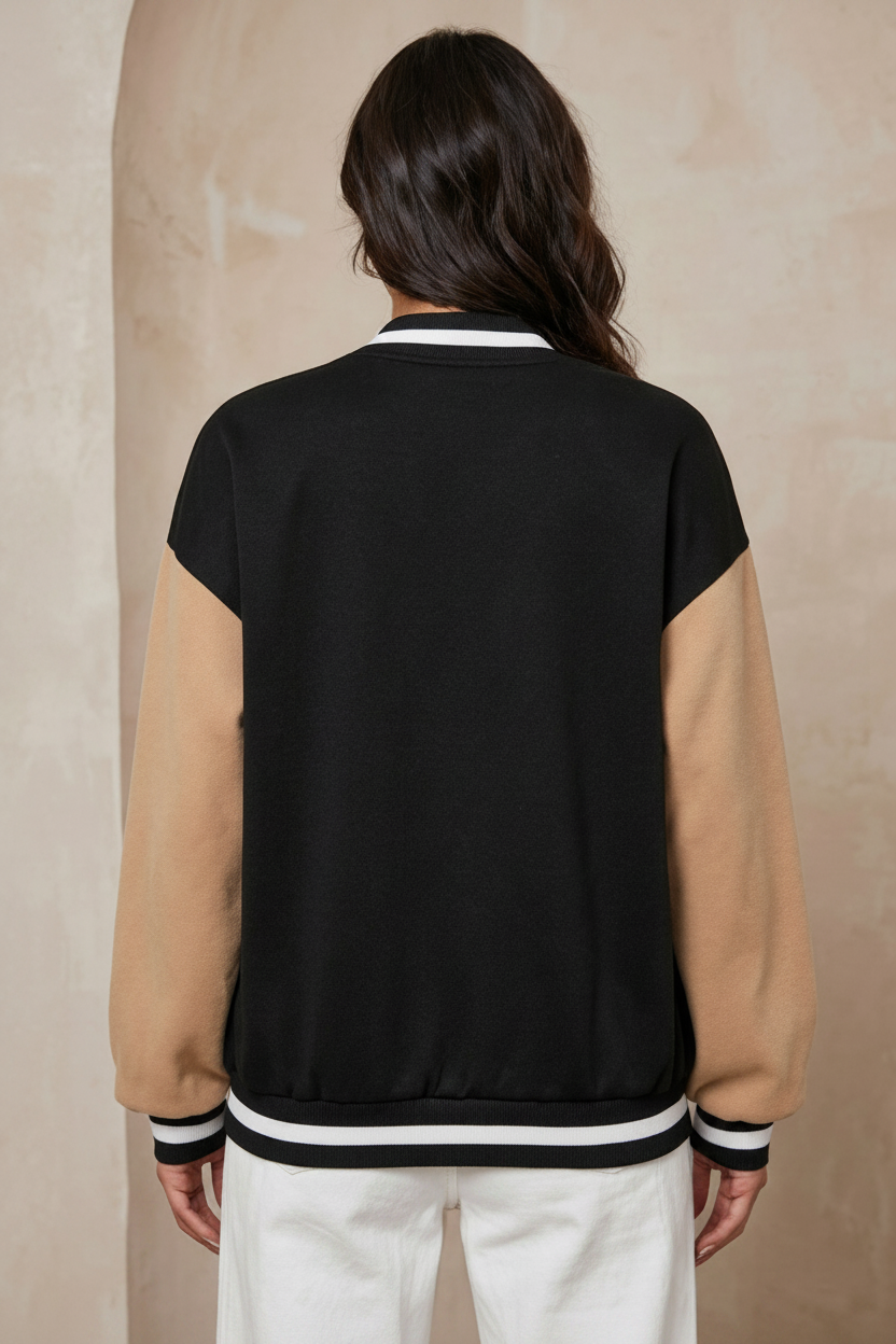 Person wearing a black and beige varsity jacket on a beige background