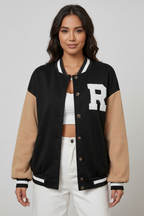 Woman wearing a black and beige varsity jacket with a large white letter 'R' on a gray background
