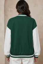 Person wearing a green and white varsity jacket against a beige background