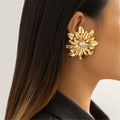 Gold floral earring with pearl center worn by a person