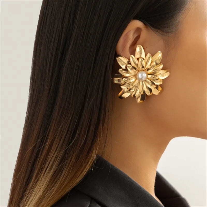 Gold floral earring with pearl center worn by a person