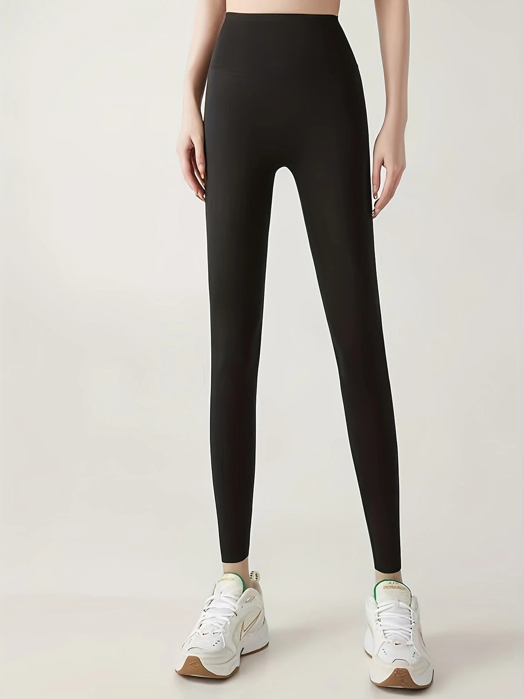 Person wearing black leggings with white sneakers on a light gray background
