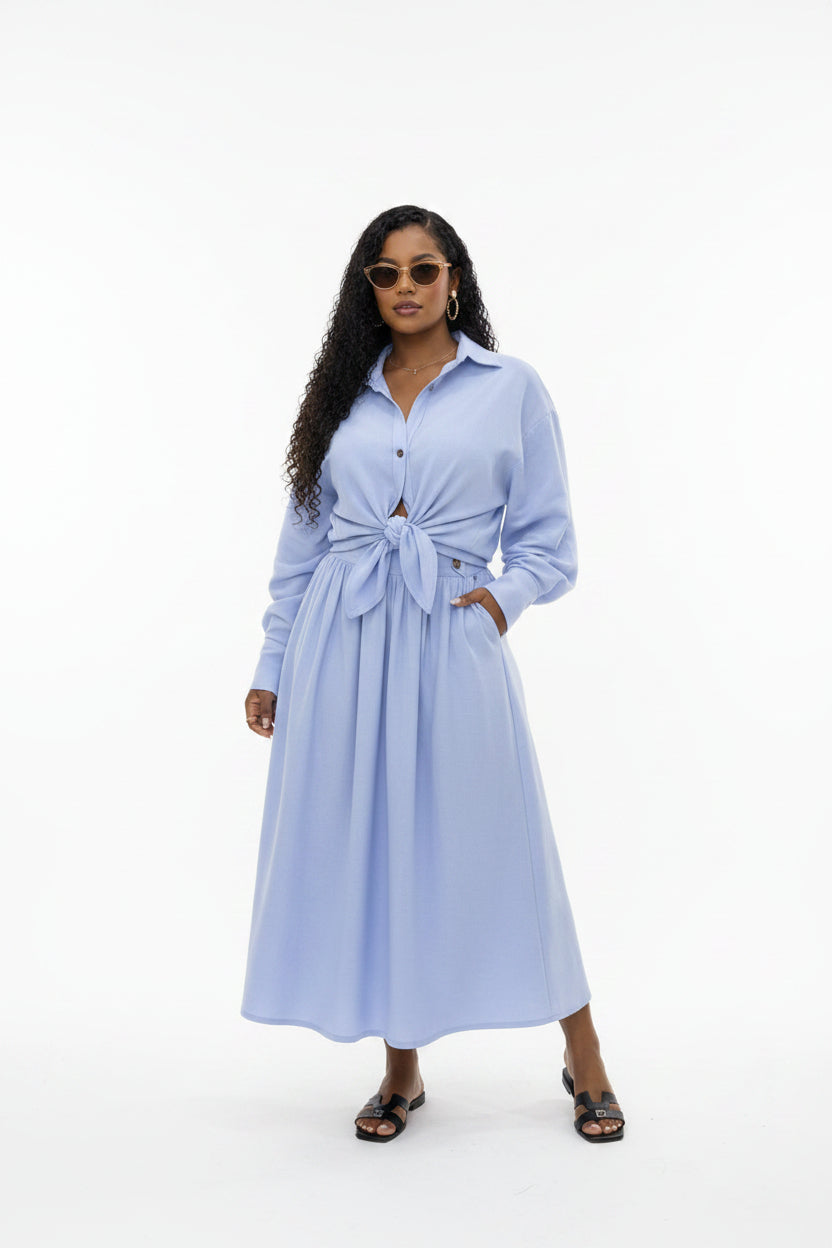 Woman wearing a light blue outfit with a long cardigan and skirt in a white background