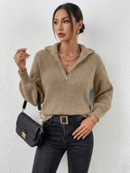 Person wearing a beige knitted sweater and black pants against a white background