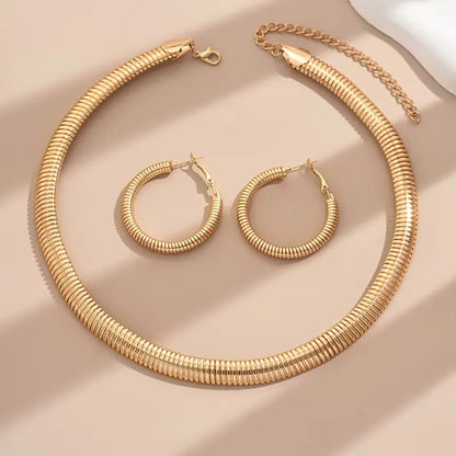 Gold necklace and hoop earrings on a beige surface