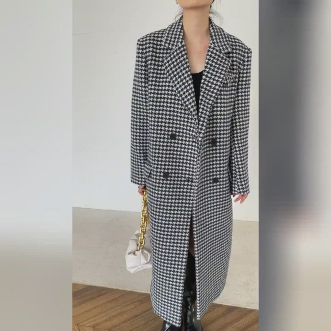 Person wearing a long houndstooth pattern coat in an indoor setting.