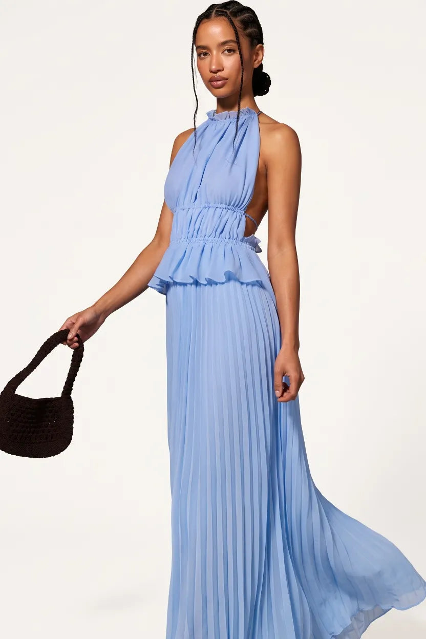 A woman models a light blue halter-neck maxi dress with a ruffled peplum waist and pleated skirt, holding a dark brown woven handbag against a plain white studio background.