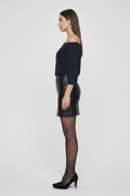 Woman wearing a black off-shoulder top, black leather skirt, and black tights on a white background