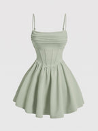 A light sage green mini dress with thin spaghetti straps, a ruched sweetheart bodice, and a flared skirt, shown against a plain light gray background.
