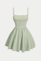 A light sage green spaghetti-strap mini dress with a fitted bodice and flared skirt, shown against a plain light gray background.