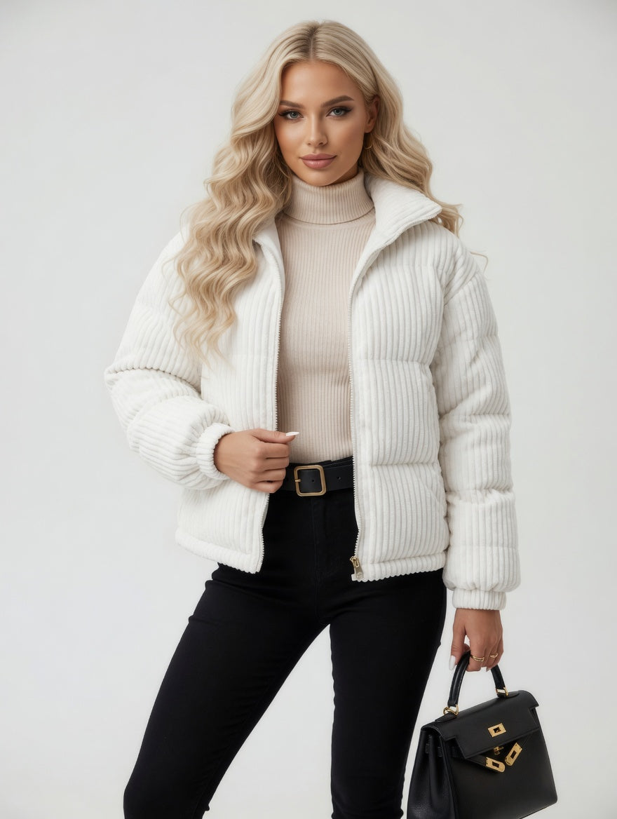 Woman wearing a white puffer jacket, beige turtleneck, black pants, and holding a black handbag on a light gray background.