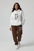 Woman wearing a white hoodie and brown sweatpants with 'RELAX' text.
