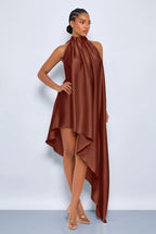 A model wearing a high-neck, high-low satin dress in a warm rust brown color, posed against a light gray studio background.