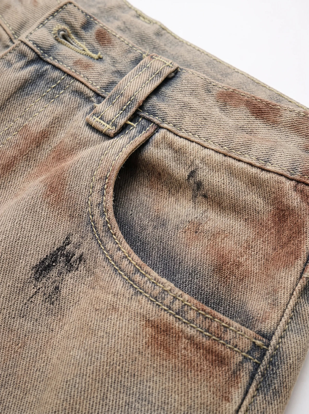 A  pair of high-waisted, curved barrel-leg jeans is crafted from a vintage-washed light khaki or beige denim adorned with an abstract, artistic spray-paint effect featuring mottled splotches of warm rust brown and distressed charcoal black.
