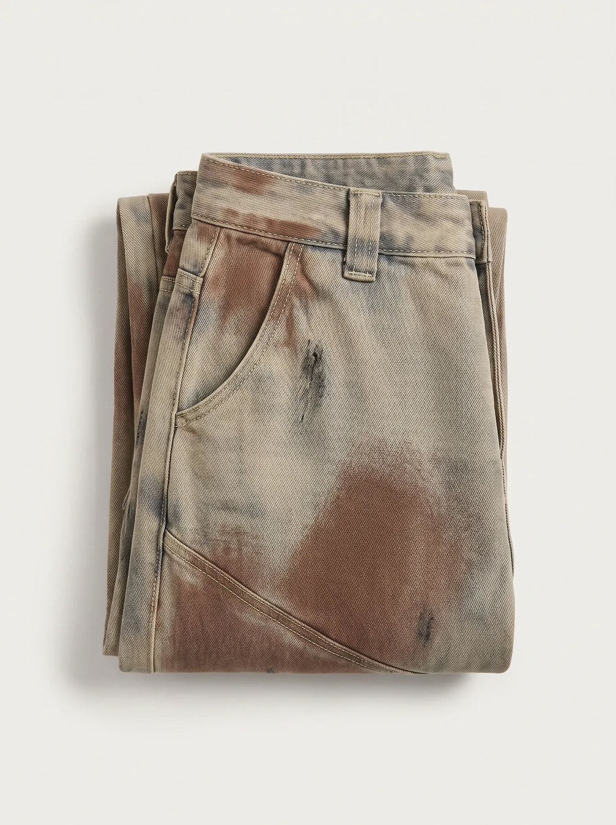 A  pair of high-waisted, curved barrel-leg jeans is crafted from a vintage-washed light khaki or beige denim adorned with an abstract, artistic spray-paint effect featuring mottled splotches of warm rust brown and distressed charcoal black.