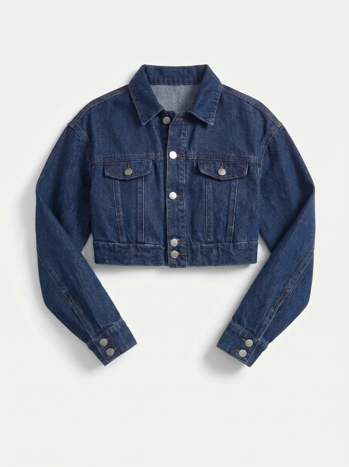 This is a deep indigo blue denim jacket features an ultra-cropped silhouette with long sleeves, tailored shoulder seams, and classic buttoned cuffs. It includes a traditional point collar and a full front placket detailed with smooth, metallic silver shank buttons.