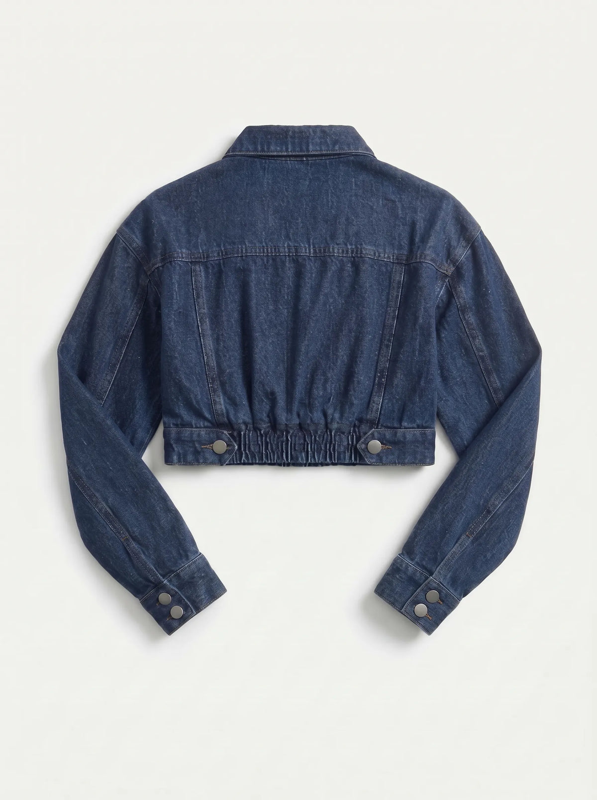This is a deep indigo blue denim jacket features an ultra-cropped silhouette with long sleeves, tailored shoulder seams, and classic buttoned cuffs. It includes a traditional point collar and a full front placket detailed with smooth, metallic silver shank buttons.