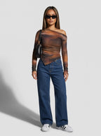 Model wearing a long-sleeved, one-shoulder top is crafted from a sheer, lightweight mesh fabric featuring an abstract, smoky watercolor print in rich tones of warm rust orange, deep brown, and muted charcoal. The fitted, asymmetrical design features soft all-over ruching that contours the body, complemented by a sleek one-shoulder neckline and a uniquely curved, lettuce-edge hemline