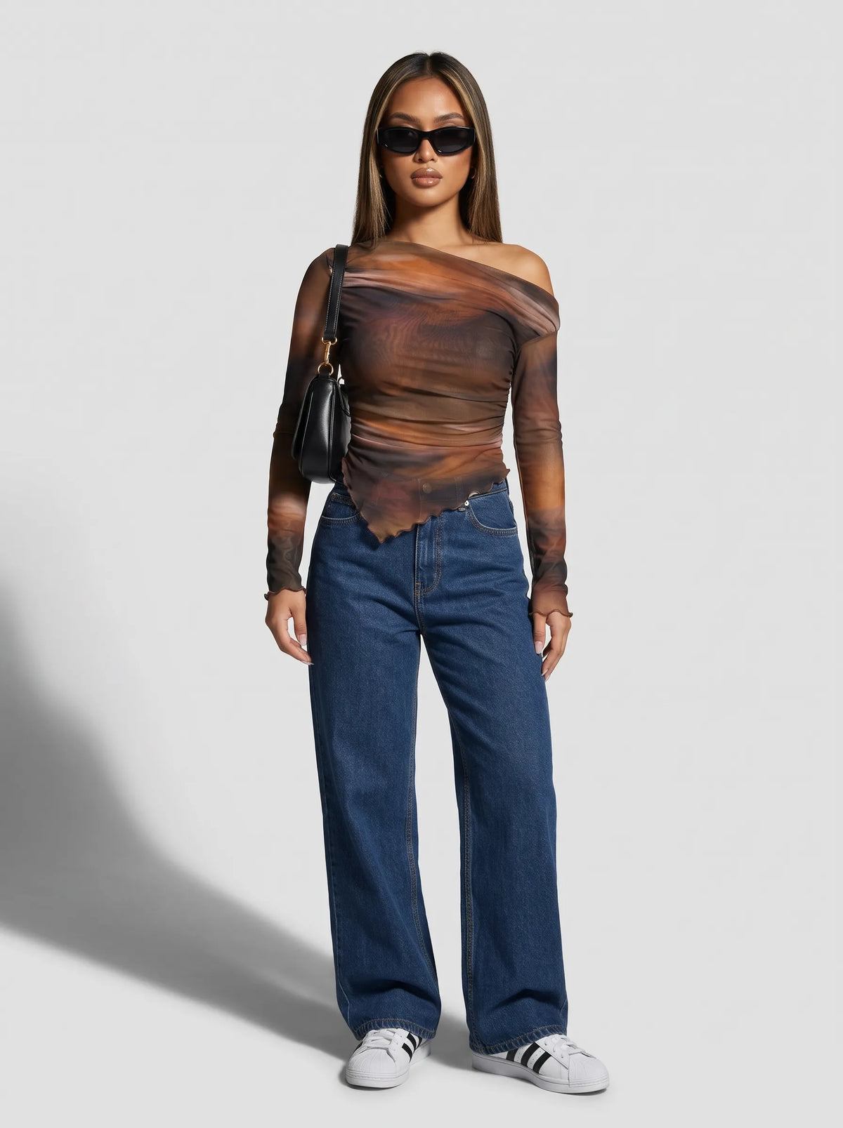Model wearing a long-sleeved, one-shoulder top is crafted from a sheer, lightweight mesh fabric featuring an abstract, smoky watercolor print in rich tones of warm rust orange, deep brown, and muted charcoal. The fitted, asymmetrical design features soft all-over ruching that contours the body, complemented by a sleek one-shoulder neckline and a uniquely curved, lettuce-edge hemline