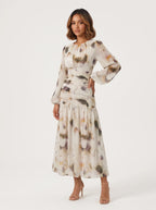 long midi dress crafted from a sheer, flowing fabric featuring an abstract, watercolor-inspired floral print in muted tones of cream, muted purple, sage, and warm amber. 