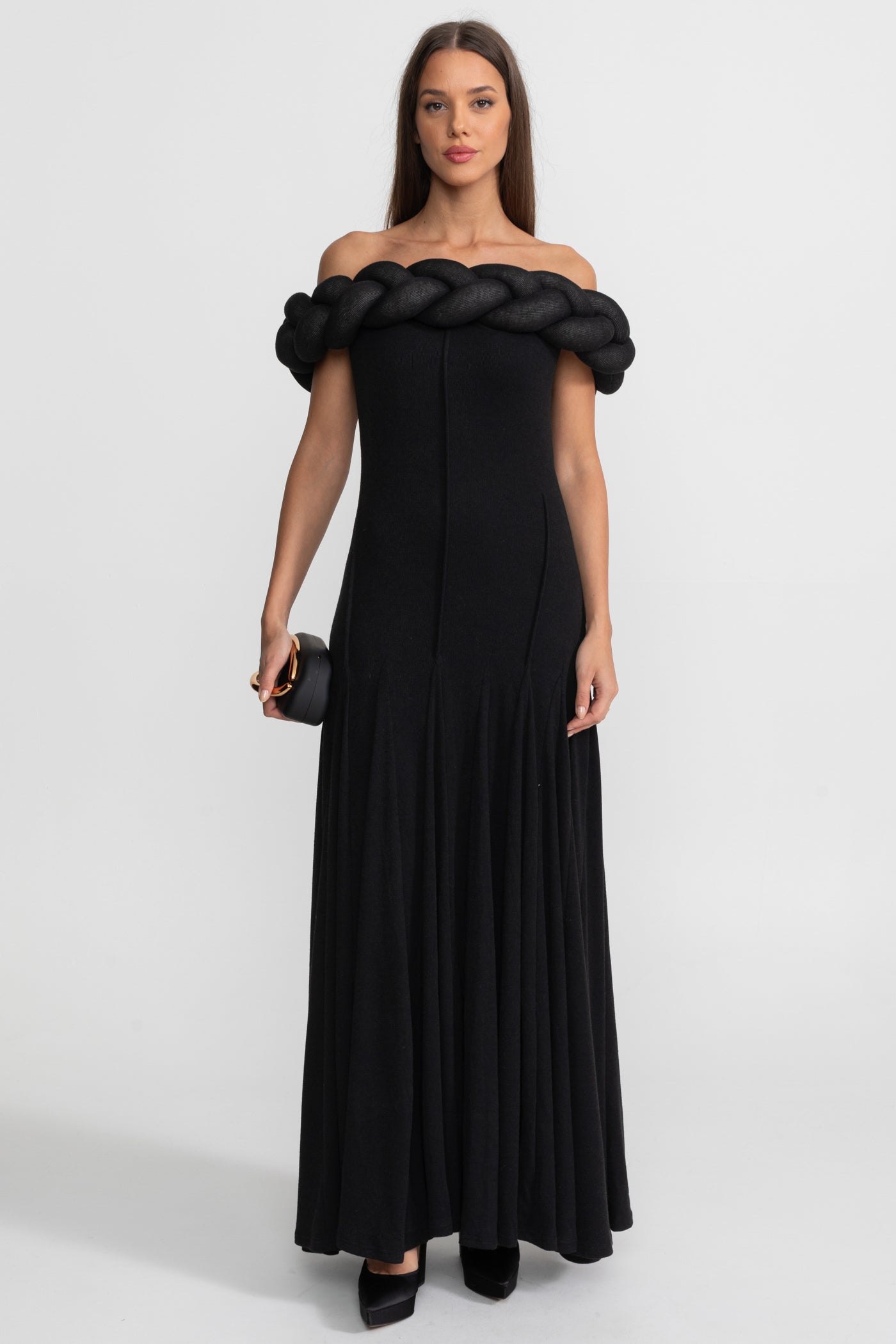 Woman wearing a black off-shoulder dress with braided detailing on a white background