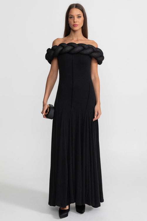 Woman wearing a black off-shoulder dress with braided detailing on a white background