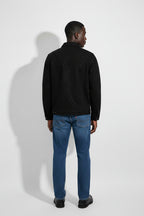 Person wearing a black jacket and blue jeans against a white background