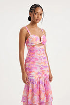 This is a vibrant maxi dress features an all-over abstract watercolor floral print in shades of pink, orange, purple, and yellow on a light background. It is designed with a sweetheart bustier-style top with sweetheart cutout at the center bust, thin shoulder straps, and a front waist cutout.