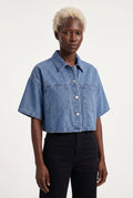 This is a medium-wash denim short-sleeved cropped jacket features a boxy, modern silhouette with relaxed drop shoulders and wide, elbow-length sleeves with stitched turned hems.