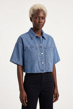 This is a medium-wash denim short-sleeved cropped jacket features a boxy, modern silhouette with relaxed drop shoulders and wide, elbow-length sleeves with stitched turned hems.